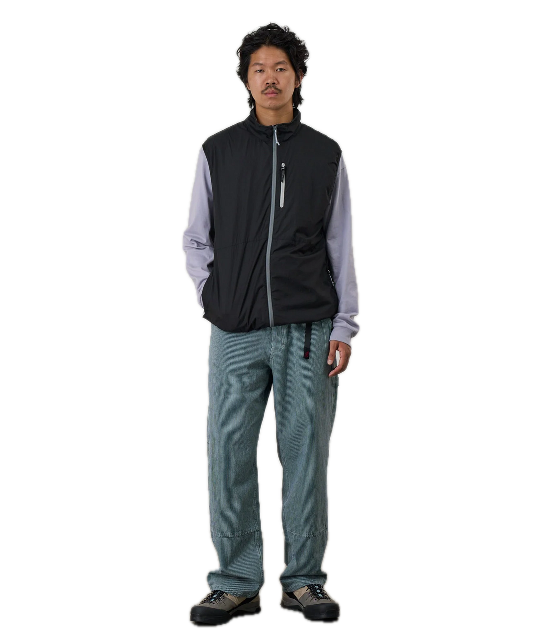 Person wearing a black vest over a light gray shirt with blue pants 