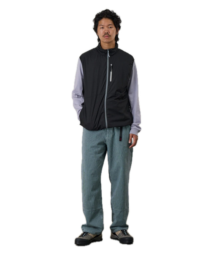 Person wearing a black vest over a light gray shirt with blue pants 