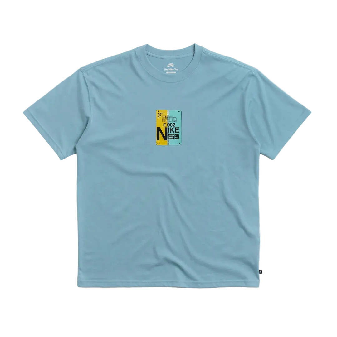 A light blue crewneck t-shirt with a small graphic print on the center chest featuring the word 'NIKE' in yellow and black, displayed on a light gray background.