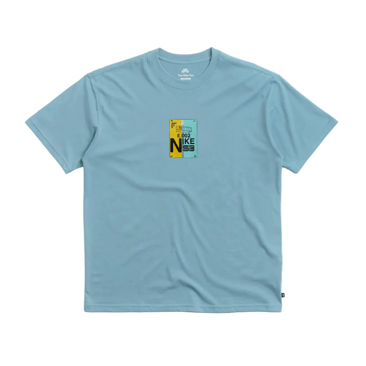 A light blue crewneck t-shirt with a small graphic print on the center chest featuring the word 'NIKE' in yellow and black, displayed on a light gray background.