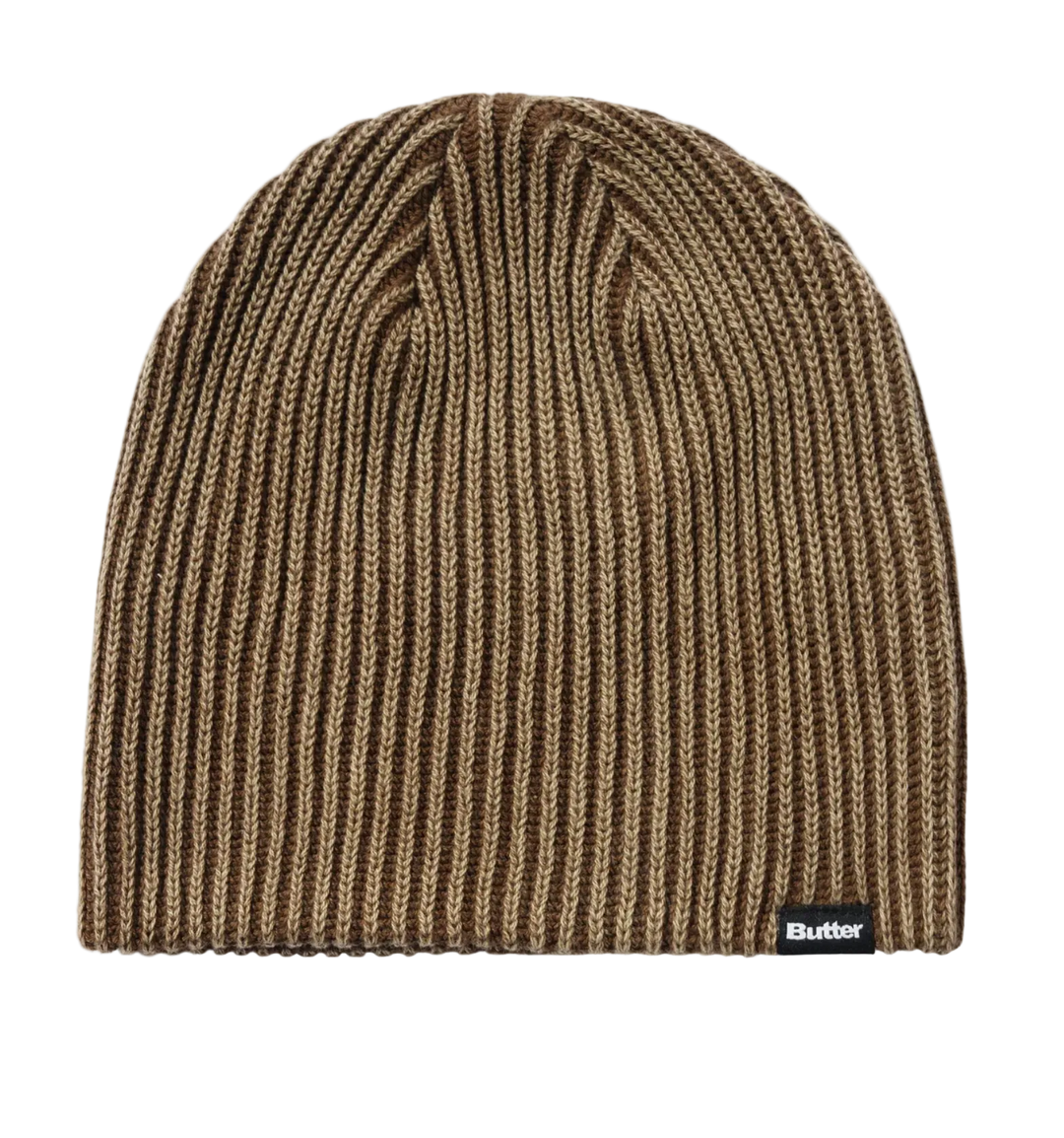 A brown and beige vertically ribbed knit beanie hat with a small black Butter brand tag on the lower right edge