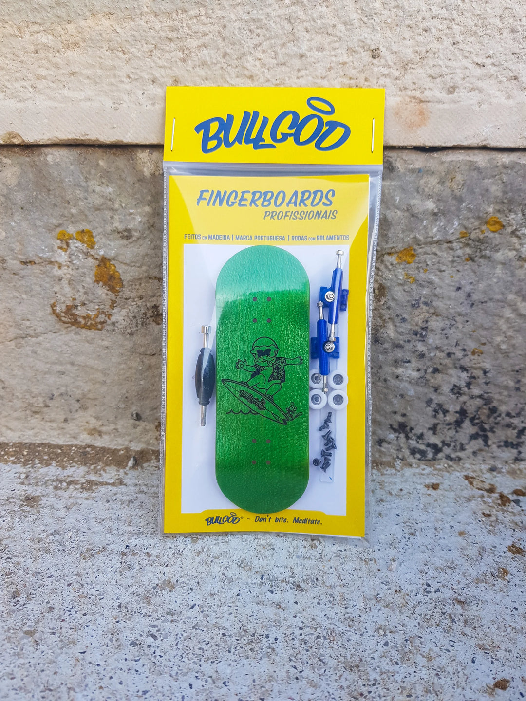A green fingerboard set inside a yellow package labeled 'BullGod Fingerboards'. The set includes a fingerboard, tape, stickers, and additional extras.